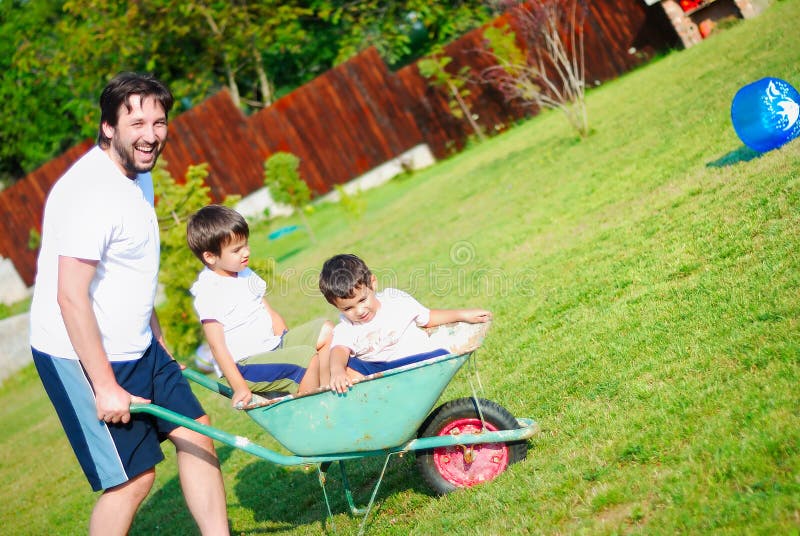 Μπαμπάς στο λευκό που οδηγεί τα αγόρια του wheelbarrow στοκ εικόνες