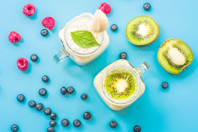 Μπανάνα δύο και ακτινίδιο milkshakes στα βάζα κτιστών με creme στην κορυφή που διακοσμείται με τα σμέουρα και τα βακκίνια επίπεδο στοκ εικόνες Μπανάνα δύο και ακτινίδιο milkshakes στα βάζα κτιστών με creme στην κορυφή που διακοσμείται με τα σμέουρα και τα βακκίνια επίπεδο στοκ εικόνες