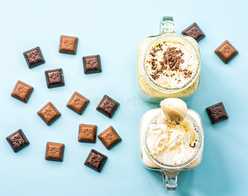 Μπανάνα δύο και ακτινίδιο milkshakes στα βάζα κτιστών με creme στην κορυφή που διακοσμείται με τα κομμάτια σοκολάτας διεσπαρμένα στοκ εικόνα Μπανάνα δύο και ακτινίδιο milkshakes στα βάζα κτιστών με creme στην κορυφή που διακοσμείται με τα κομμάτια σοκολάτας διεσπαρμένα στοκ εικόνα