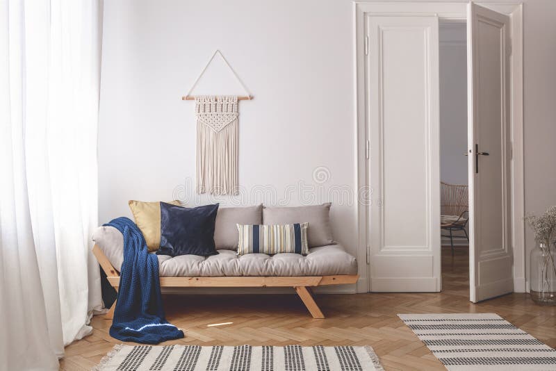 Blue blanket and pillows on wooden couch in white living room interior with rugs and door. Real photo concept. Blue blanket and pillows on wooden couch in white living room interior with rugs and door. Real photo concept