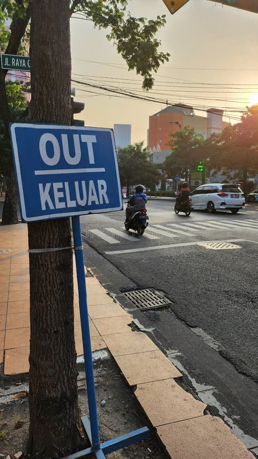 Μπλε και λευκό σήμα που δείχνει OUT και KELUAR και δείχνει ότι μια έξοδος είναι τοποθετημένη σε ένα δέντρο δίπλα σε έναν δρόμο στη στοκ εικόνες
