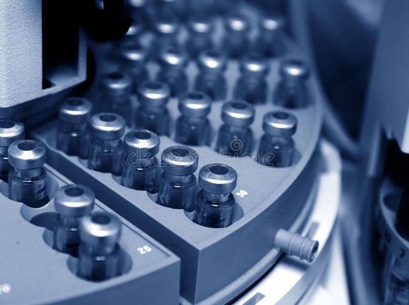 Capped vials on an analysis autosampler - selective focus, blue tinting. Capped vials on an analysis autosampler - selective focus, blue tinting