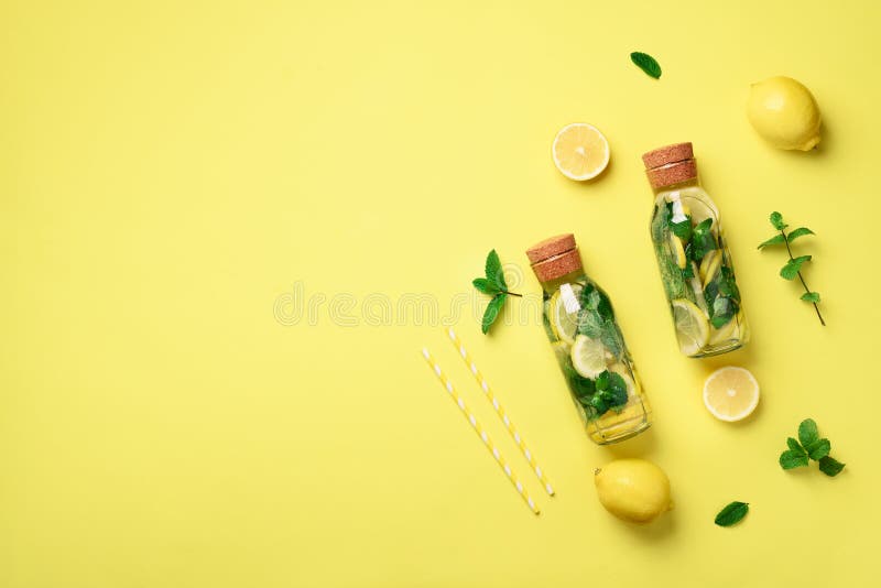 Bottle of detox water with mint, lemon on yellow background. Flat lay. Citrus lemonade. Summer fruit infused water. Top view with copy space. Bottle of detox water with mint, lemon on yellow background. Flat lay. Citrus lemonade. Summer fruit infused water. Top view with copy space
