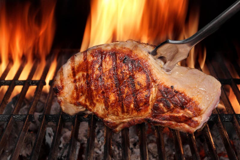 Browned Pork Loin Steak On The Hot Barbecue Charcoal Grill With Fork, Bright Flames Of Fire On The Black Background, Close Up, Front View, Cookout Food For Outdoor Party Or Picnic. Browned Pork Loin Steak On The Hot Barbecue Charcoal Grill With Fork, Bright Flames Of Fire On The Black Background, Close Up, Front View, Cookout Food For Outdoor Party Or Picnic