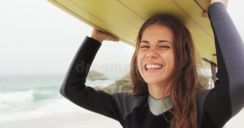 Μπροστινή άποψη της καυκάσιας θηλυκής φέρνοντας ιστιοσανίδας surfer στο κεφάλι της στην παραλία 4k