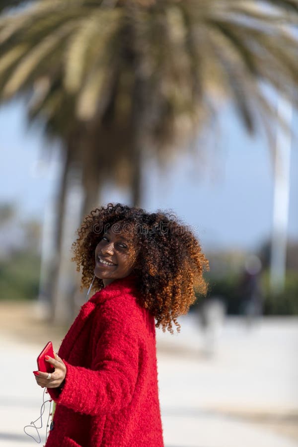 Μπροστινή άποψη της νέας στάσης γυναικών afro χαμόγελου σγουρής υπαίθρι στοκ εικόνα Μπροστινή άποψη της νέας στάσης γυναικών afro χαμόγελου σγουρής υπαίθρι στοκ εικόνα