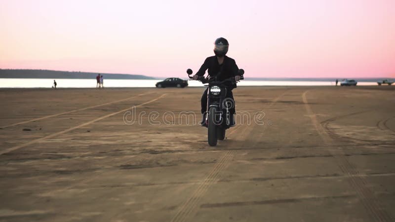 Μπροστινή όψη του νεαρού μηχανόβιου με κράνος και μπουφάν, ο άνθρωπος οδηγεί σε αθλητική μοτοσικλέτα Φυσάει αέρα, νερό μπροστά
