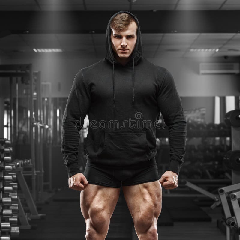 Μυϊκό άτομο με τα πόδια μυών στη γυμναστική Ισχυρό αρσενικό στο μαύρο hoodie με τα μεγάλα τετράγωνα