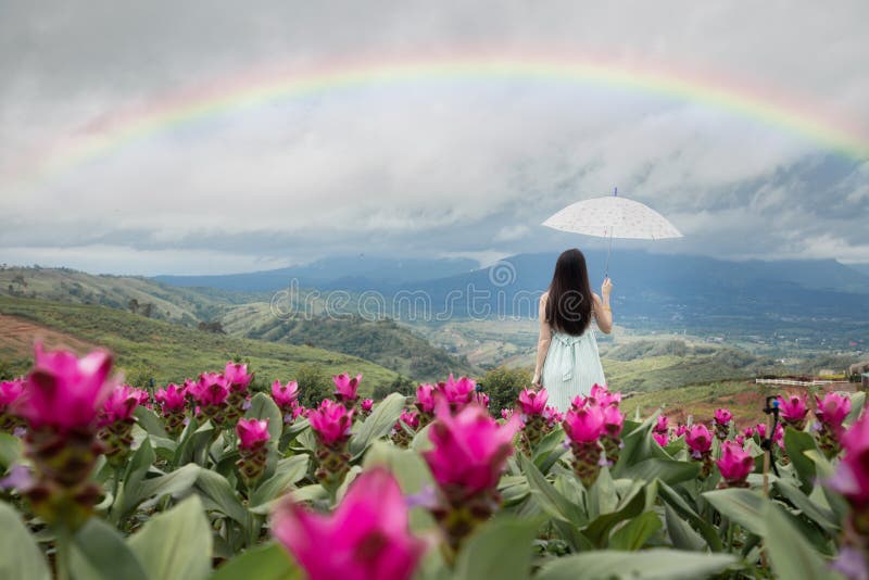 Μόνη γυναίκα που κρατά ομπρέλα με όμορφο ουράνιο τόξο στον κήπο με τα λουλούδια, πίσω όψη