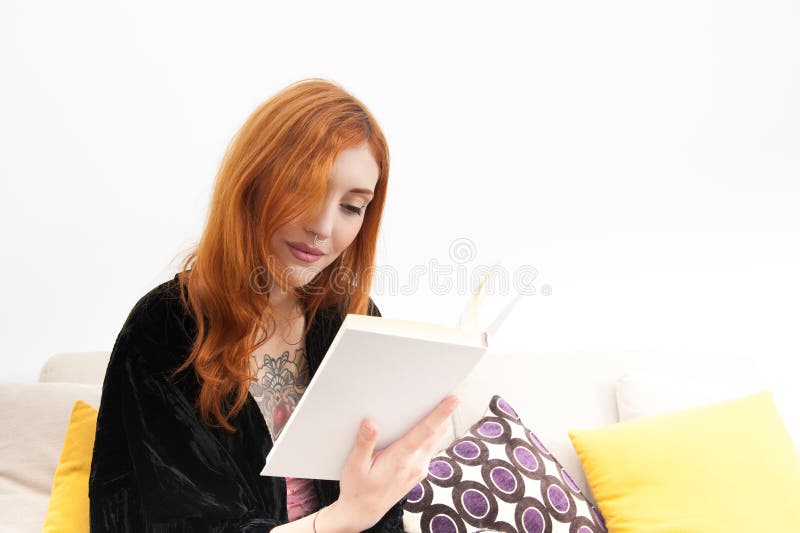 Νέα redhead γυναίκα που χαμογελά και που διαβάζει ένα βιβλίο στοκ εικόνα Νέα redhead γυναίκα που χαμογελά και που διαβάζει ένα βιβλίο στοκ εικόνα
