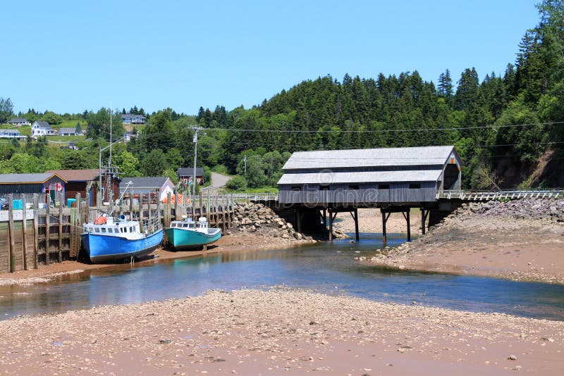 Fishing wharf in St. Martins, New Brunswick, Canada on low tide with moored boats in mud with a covered bridge in the background. Fishing wharf in St. Martins, New Brunswick, Canada on low tide with moored boats in mud with a covered bridge in the background