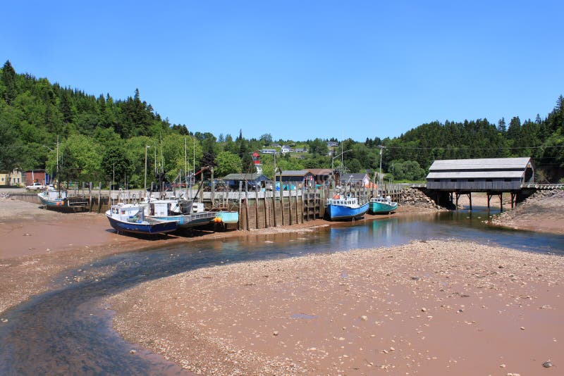 Fishing wharf in St. Martins, New Brunswick, Canada on low tide with moored boats in mud with a covered bridge in the background. Fishing wharf in St. Martins, New Brunswick, Canada on low tide with moored boats in mud with a covered bridge in the background