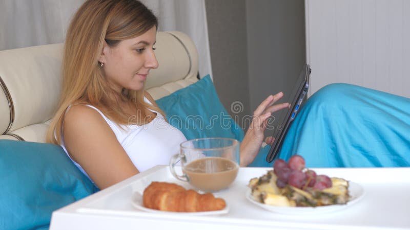 Νέα γυναίκα με το lap-top που τρώει το πρόγευμα στο κρεβάτι στο σπίτι και τον καφέ κατανάλωσης στοκ φωτογραφία με δικαίωμα ελεύθερης χρήσης Νέα γυναίκα με το lap-top που τρώει το πρόγευμα στο κρεβάτι στο σπίτι και τον καφέ κατανάλωσης στοκ φωτογραφία με δικαίωμα ελεύθερης χρήσης