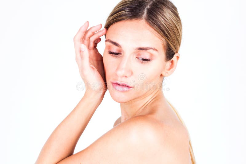 Νέα γυναίκα με το ομαλό δέρμα που κρατά το χέρι της κοντά στο μάγουλο και που κοιτάζει κάτω