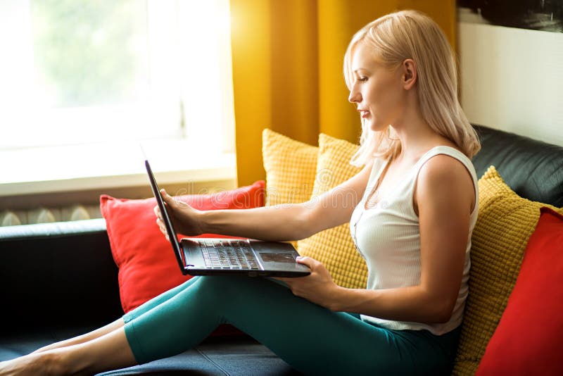Νέα γυναίκα που χρησιμοποιεί το lap-top χαλαρώνοντας στον καναπέ στοκ φωτογραφία με δικαίωμα ελεύθερης χρήσης Νέα γυναίκα που χρησιμοποιεί το lap-top χαλαρώνοντας στον καναπέ στοκ φωτογραφία με δικαίωμα ελεύθερης χρήσης