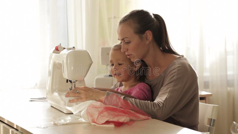 Νέα ελκυστική μητέρα που απασχολείται στη ράβοντας μηχανή με την σε λίγη χαριτωμένη κόρη