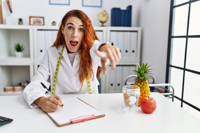 Young redhead woman nutritionist doctor at the clinic pointing displeased and frustrated to the camera, angry and furious with you. Young redhead woman nutritionist doctor at the clinic pointing displeased and frustrated to the camera, angry and furious with you