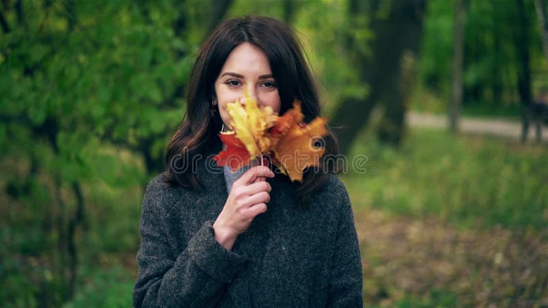 Νέα κυματίζοντας φύλλα σφενδάμου γυναικών κοντά στο πρόσωπό της στο πάρκο φθινοπώρου