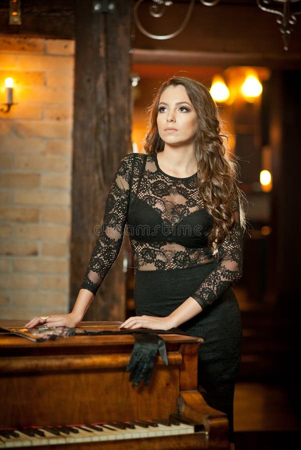 Νέα όμορφη γυναίκα brunette στο κομψό μαύρο φόρεμα που στέκεται κοντά σε ένα εκλεκτής ποιότητας πιάνο Αισθησιακή ρομαντική κυρία στοκ φωτογραφία Νέα όμορφη γυναίκα brunette στο κομψό μαύρο φόρεμα που στέκεται κοντά σε ένα εκλεκτής ποιότητας πιάνο Αισθησιακή ρομαντική κυρία στοκ φωτογραφία