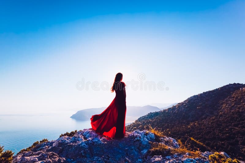 Νέα όμορφη γυναίκα στο κόκκινο φόρεμα που κοιτάζει στη θάλασσα βουνών στοκ φωτογραφία Νέα όμορφη γυναίκα στο κόκκινο φόρεμα που κοιτάζει στη θάλασσα βουνών στοκ φωτογραφία