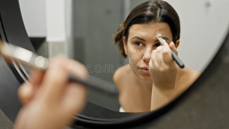 νέα όμορφη ισπανόφωνη γυναίκα που κάνει αίτηση κάνει μέικ απ στο μπάνιο στοκ εικόνες