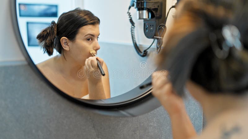 νέα όμορφη ισπανόφωνη γυναίκα που κάνει αίτηση κάνει μέικ απ στο μπάνιο στοκ φωτογραφία