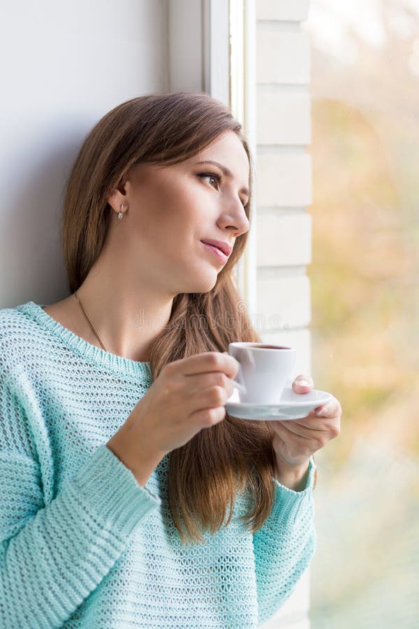 Νέα όμορφη καυκάσια γυναίκα που πίνει το espresso της στη στρωματοειδή φλέβα παραθύρων στοκ φωτογραφία Νέα όμορφη καυκάσια γυναίκα που πίνει το espresso της στη στρωματοειδή φλέβα παραθύρων στοκ φωτογραφία