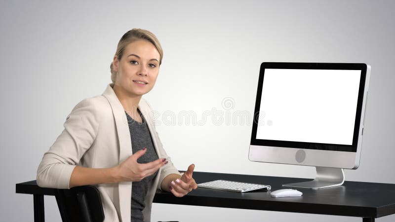 Νέα όμορφη κυρία που μιλά στη κάμερα και που παρουσιάζει κάτι στην οθόνη του υπολογιστή στο υπόβαθρο κλίσης στοκ εικόνα Νέα όμορφη κυρία που μιλά στη κάμερα και που παρουσιάζει κάτι στην οθόνη του υπολογιστή στο υπόβαθρο κλίσης στοκ εικόνα