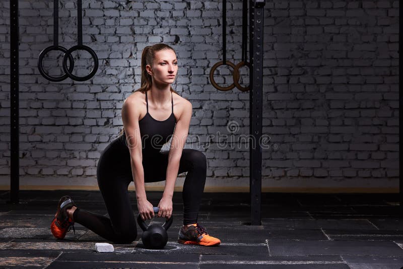 Νέα όμορφη φίλαθλη εκμετάλλευση γυναικών kettlebell στο πάτωμα γυμναστικής ενάντια στο τουβλότοιχο στοκ φωτογραφίες με δικαίωμα ελεύθερης χρήσης Νέα όμορφη φίλαθλη εκμετάλλευση γυναικών kettlebell στο πάτωμα γυμναστικής ενάντια στο τουβλότοιχο στοκ φωτογραφίες με δικαίωμα ελεύθερης χρήσης