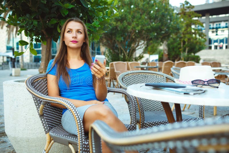 Νέα όμορφη χαλάρωση γυναικών στον υπαίθριο καφέ και χρησιμοποίηση smartp στοκ φωτογραφία με δικαίωμα ελεύθερης χρήσης Νέα όμορφη χαλάρωση γυναικών στον υπαίθριο καφέ και χρησιμοποίηση smartp στοκ φωτογραφία με δικαίωμα ελεύθερης χρήσης