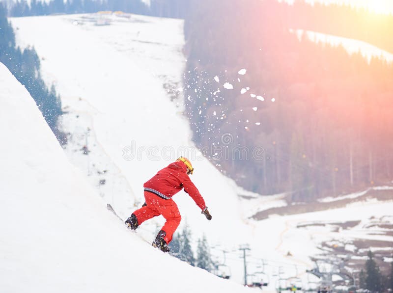 Νέο αρσενικό snowboarder που οδηγά από την κορυφή του χιονώδους λόφου με το σνόουμπορντ στο ηλιοβασίλεμα στο χιονοδρομικό κέντρο στοκ εικόνα με δικαίωμα ελεύθερης χρήσης Νέο αρσενικό snowboarder που οδηγά από την κορυφή του χιονώδους λόφου με το σνόουμπορντ στο ηλιοβασίλεμα στο χιονοδρομικό κέντρο στοκ εικόνα με δικαίωμα ελεύθερης χρήσης