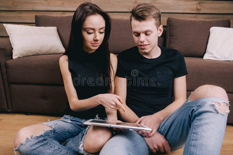 Νέο ζεύγος sittng στο πάτωμα σε μια κρεβατοκάμαρα και χρησιμοποίηση της ψηφιακής ταμπλέτας στοκ εικόνα με δικαίωμα ελεύθερης χρήσης Νέο ζεύγος sittng στο πάτωμα σε μια κρεβατοκάμαρα και χρησιμοποίηση της ψηφιακής ταμπλέτας στοκ εικόνα με δικαίωμα ελεύθερης χρήσης