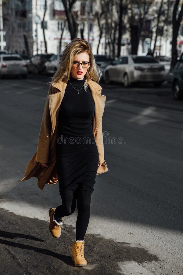Νέο κορίτσι μόδας στα γυαλιά Ξανθά, κόκκινα χείλια, μπεζ παλτό που περπατούν κατά μήκος της οδού πόλεων στοκ εικόνες Νέο κορίτσι μόδας στα γυαλιά Ξανθά, κόκκινα χείλια, μπεζ παλτό που περπατούν κατά μήκος της οδού πόλεων στοκ εικόνες
