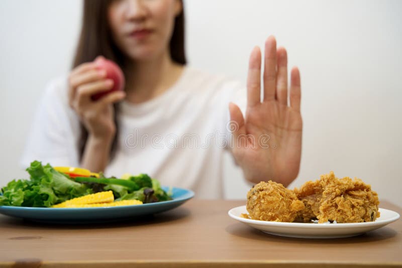 Young girl on dieting for good health concept. Close up female using hand reject junk food by pushing out her favorite fried chicken and choose red apple and salad for good health. Young girl on dieting for good health concept. Close up female using hand reject junk food by pushing out her favorite fried chicken and choose red apple and salad for good health