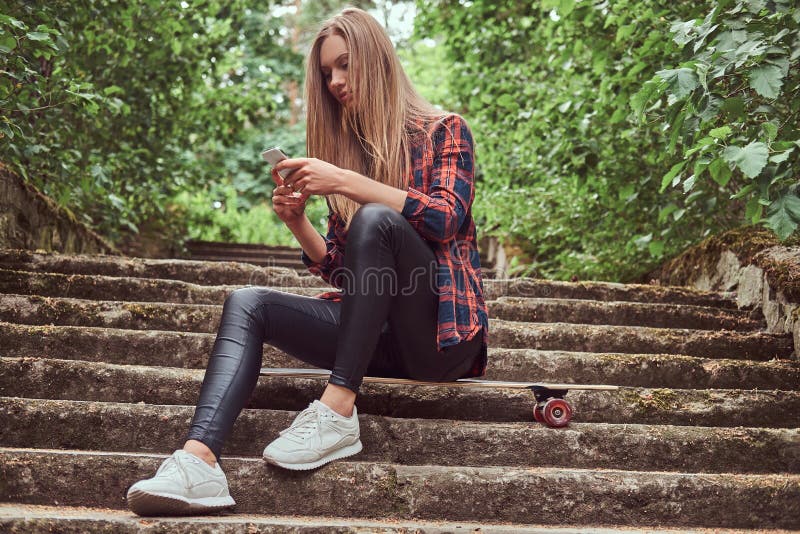 Νέο ξανθό κορίτσι hipster που χρησιμοποιεί ένα smartphone καθμένος στα βήματα σε ένα πάρκο στοκ εικόνες με δικαίωμα ελεύθερης χρήσης Νέο ξανθό κορίτσι hipster που χρησιμοποιεί ένα smartphone καθμένος στα βήματα σε ένα πάρκο στοκ εικόνες με δικαίωμα ελεύθερης χρήσης