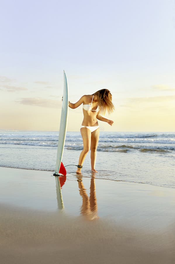 Νέο όμορφο κορίτσι surfer που στέκεται στην παραλία με την ιστιοσανίδα στοκ φωτογραφίες