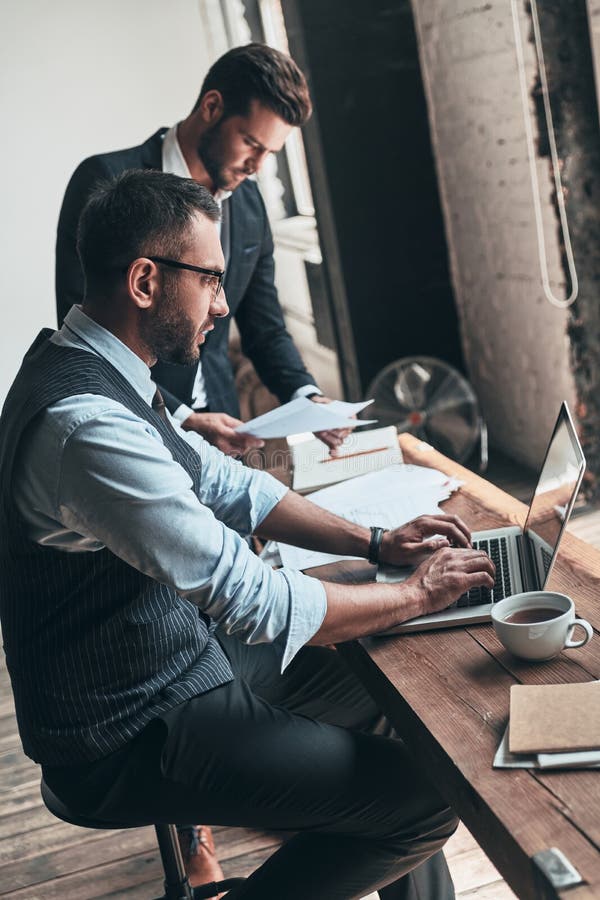 Young business professionals. Two young modern men in formalwear working together while sitting indoors. Young business professionals. Two young modern men in formalwear working together while sitting indoors