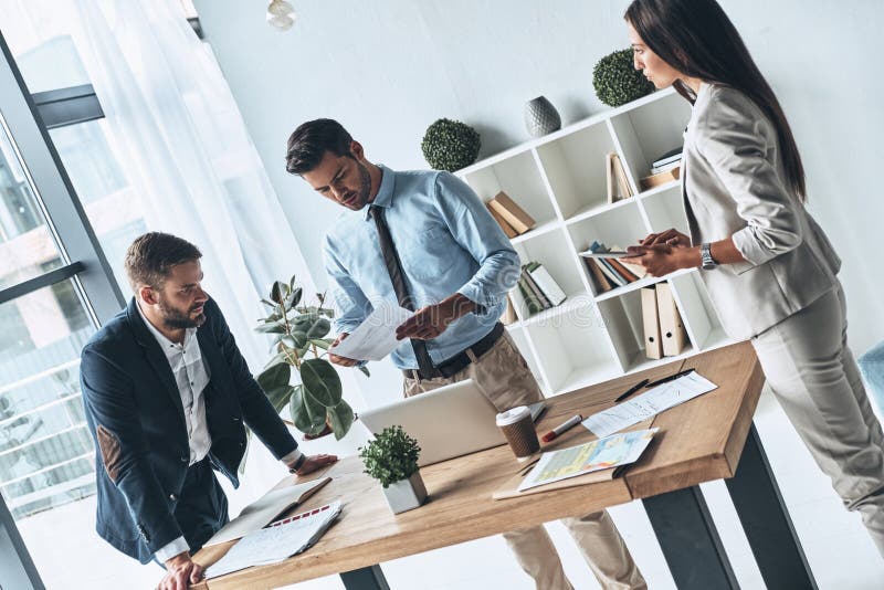 Young business professionals. Group of young modern people in smart casual wear discussing business while standing in the creative office. Young business professionals. Group of young modern people in smart casual wear discussing business while standing in the creative office