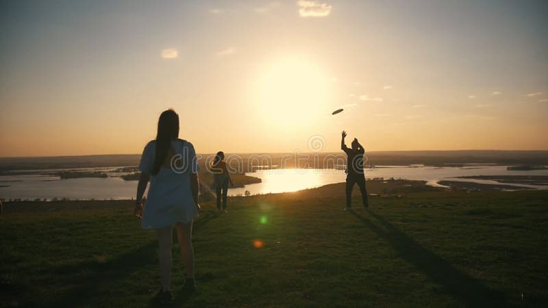 Νέοι φίλοι που παίζουν το frisbee στο λόφο στο ηλιοβασίλεμα