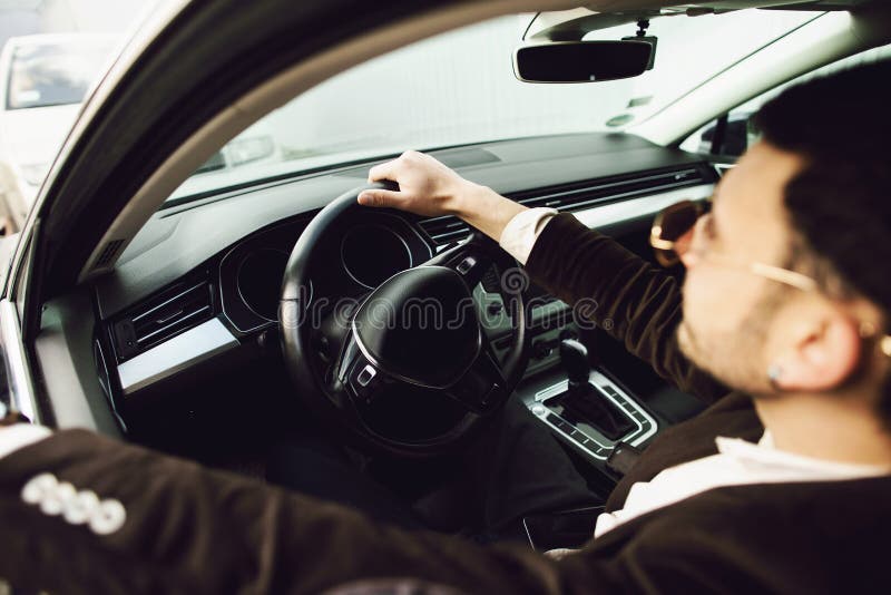 Νέος bussinesman στο κοστούμι και τα μαύρα γυαλιά που οδηγούν το αυτοκίνητό του Η επιχείρηση κοιτάζει Τεστ δοκιμής του νέου αυτοκ στοκ εικόνα με δικαίωμα ελεύθερης χρήσης Νέος bussinesman στο κοστούμι και τα μαύρα γυαλιά που οδηγούν το αυτοκίνητό του Η επιχείρηση κοιτάζει Τεστ δοκιμής του νέου αυτοκ στοκ εικόνα με δικαίωμα ελεύθερης χρήσης