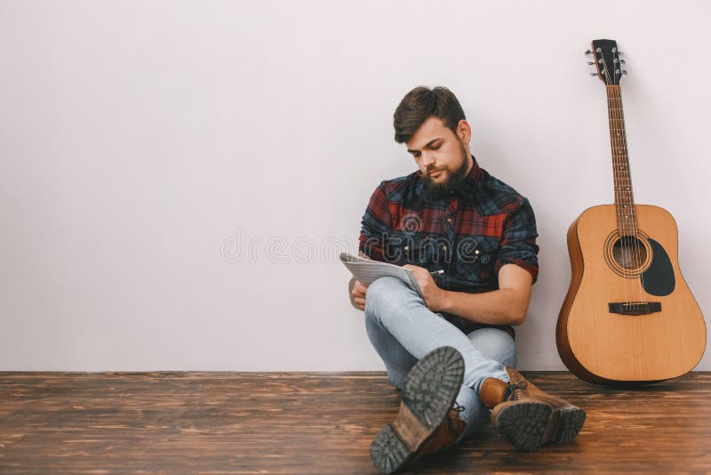 Νέος κιθαρίστας hipster στο σπίτι με τη μελωδία γραψίματος συνεδρίασης κιθάρων στοκ φωτογραφία με δικαίωμα ελεύθερης χρήσης Νέος κιθαρίστας hipster στο σπίτι με τη μελωδία γραψίματος συνεδρίασης κιθάρων στοκ φωτογραφία με δικαίωμα ελεύθερης χρήσης