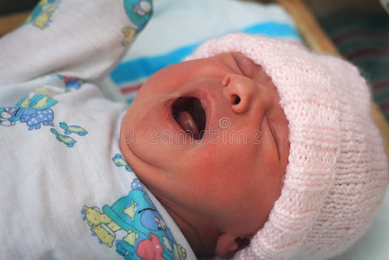 A close-up portrait of a crying newborn baby wearing a pink knitted cap. Shallow depth of field. A close-up portrait of a crying newborn baby wearing a pink knitted cap. Shallow depth of field.