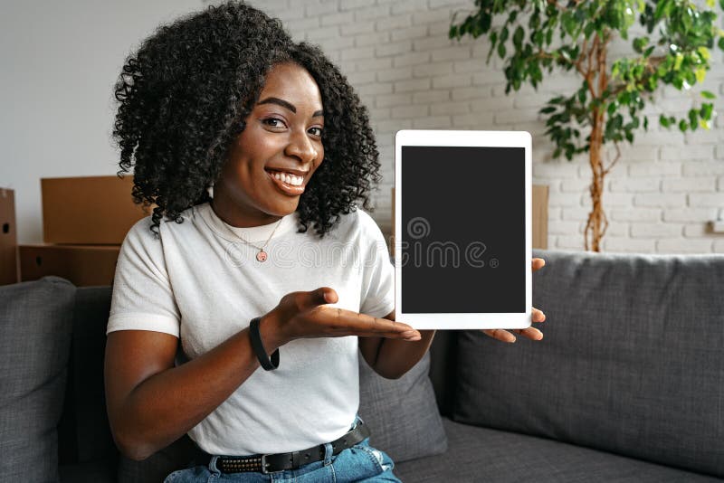 νεαρή αφρικανή που χρησιμοποιεί ένα tablet καθώς κάθεται σε σαλόνι περιτριγυρισμένη από χάρτινα κουτιά στοκ εικόνα με δικαίωμα ελεύθερης χρήσης