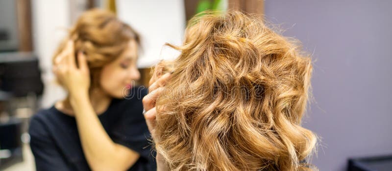 νεαρή γυναίκα που κοιτούσε το νέο σγουρό καστανό στυλ της μπροστά στον καθρέφτη στο κομμωτήριο στοκ φωτογραφία με δικαίωμα ελεύθερης χρήσης