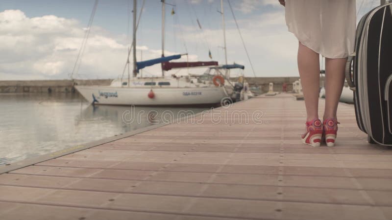 νεαρή γυναίκα που πηγαίνει διακοπές. γυναίκα με βαριά βαλίτσα. θηλυκό που περπατά μακριά στην ξύλινη γέφυρα στο λιμάνι του γιοτ φιλμ μικρού μήκους
