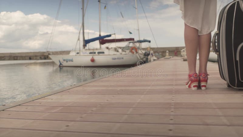 νεαρή γυναίκα που πηγαίνει διακοπές. γυναίκα με βαριά βαλίτσα. θηλυκό που περπατά μακριά στην ξύλινη γέφυρα στο λιμάνι του γιοτ φιλμ μικρού μήκους