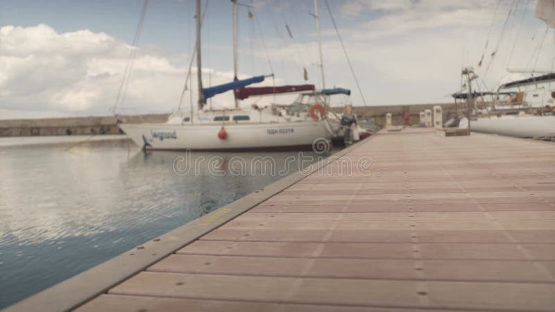 νεαρή γυναίκα που πηγαίνει διακοπές. γυναίκα με βαριά βαλίτσα. θηλυκό που περπατά μακριά στην ξύλινη γέφυρα στο λιμάνι του γιοτ απόθεμα βίντεο