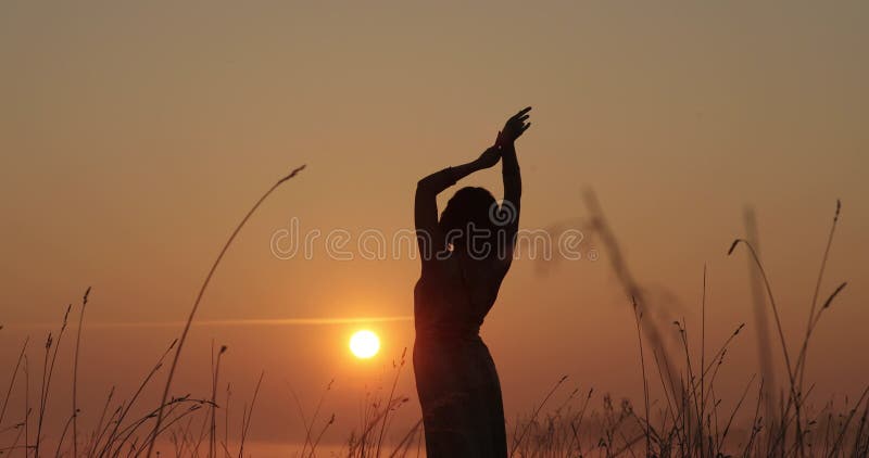 νεαρή γυναίκα σιλουέτα που χόρευε έξω σε ένα ηλιοβασίλεμα με τον ήλιο να λάμπει πίσω της σε έναν ορίζοντα. αργή κίνηση.