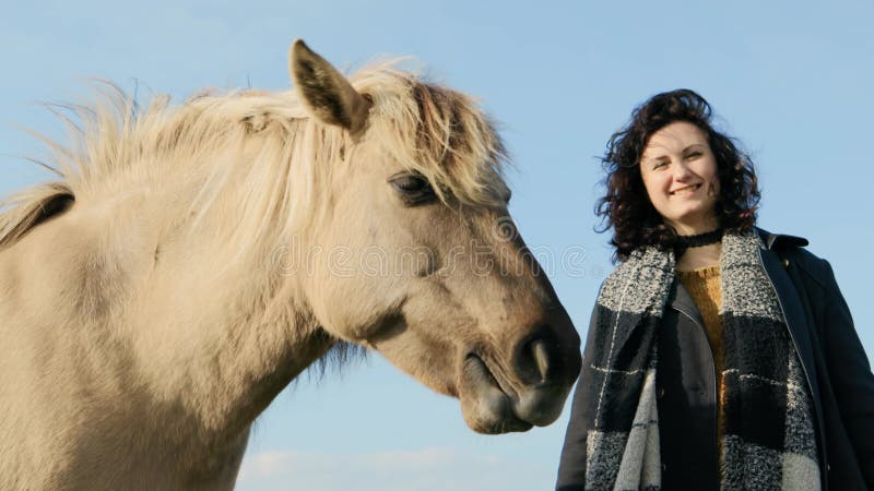 νεαρή γυναίκα χαμογελά μαζί με το άλογο konik polski ενάντια στον γαλάζιο ουρανό