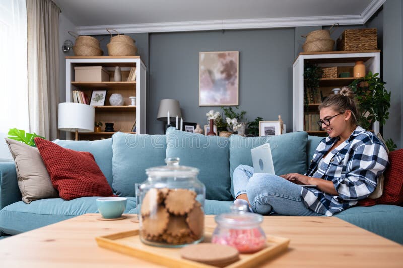 Young female freelancer in casual clothes sitting on comfortable couch and working remotely on laptop. Woman copyright writer or web developer work at home sitting on sofa enjoying her freedom. Young female freelancer in casual clothes sitting on comfortable couch and working remotely on laptop. Woman copyright writer or web developer work at home sitting on sofa enjoying her freedom